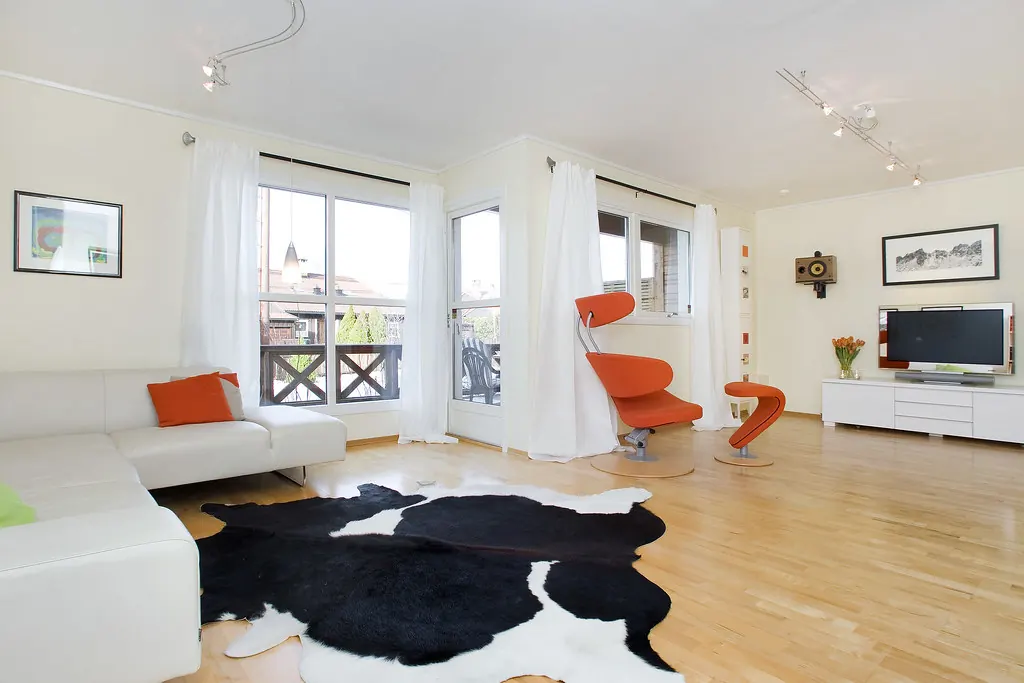 Salón blanco con sofá, alfombra de piel y butaca naranja